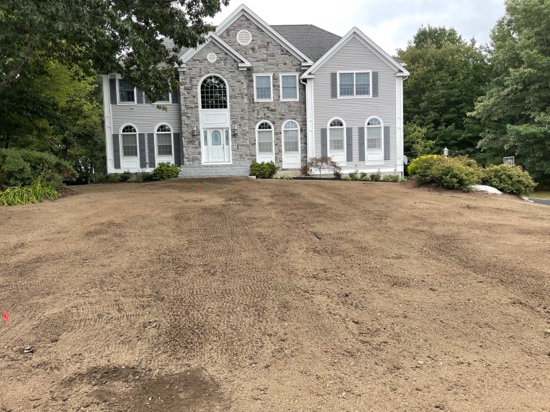 Large two-story house with stone and siding facade, surrounded by trees. The front yard is bare soil, awaiting landscaping.