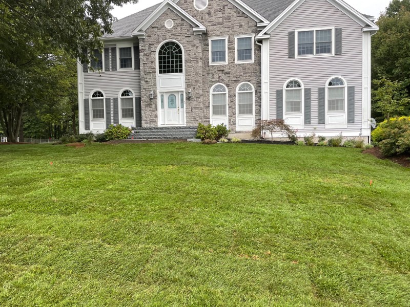 A large two-story house with a stone and gray siding facade, featuring multiple arched windows and a manicured green lawn in the foreground.